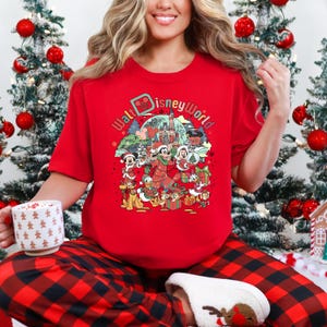 May include: Red crew neck t-shirt featuring a colorful graphic of Disney characters in a Christmas theme. The graphic includes Mickey Mouse, Minnie Mouse, Donald Duck, and Goofy, with the words "Walt Disney World" in a circular design. The shirt is paired with red and black plaid pajama pants.