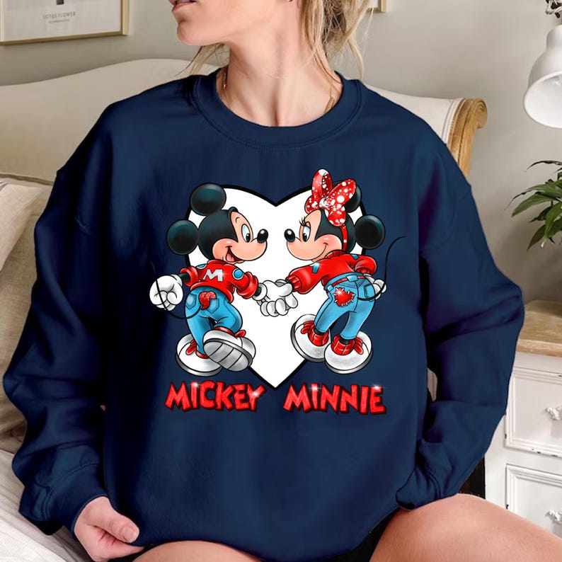 May include: A navy blue sweatshirt with a white heart graphic featuring Mickey Mouse and Minnie Mouse in red and blue outfits. The text "Mickey Minnie" is printed below the heart.