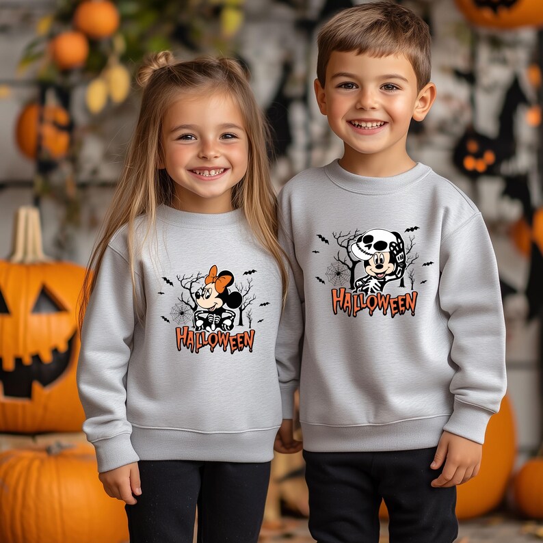 May include: Two children wearing matching light gray Halloween sweatshirts. One sweatshirt features Minnie Mouse in a skeleton costume, the other features Mickey Mouse in a skeleton costume. Both sweatshirts have the word "Halloween" in orange.