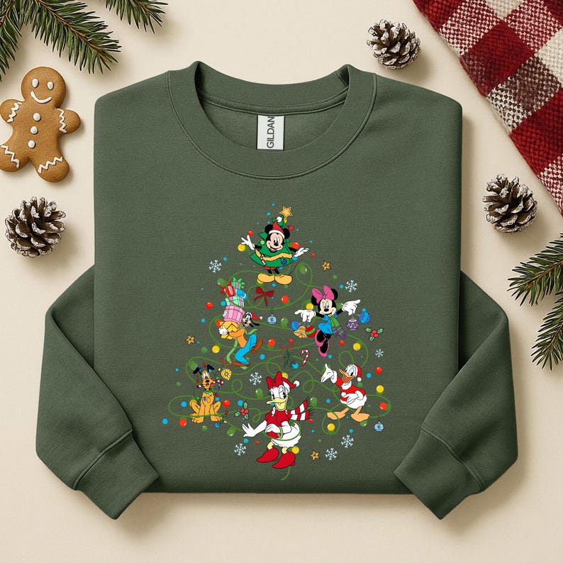 K&ouml;nnte beinhalten: Gr&uuml;nes Sweatshirt mit einem Weihnachtsbaum-Design aus Disney-Figuren, darunter Mickey und Minnie Mouse sowie Donald Duck. Das Design umfasst bunte Ornamente und einen Stern. Das Sweatshirt hat einen Rundhalsausschnitt und lange &Auml;rmel.