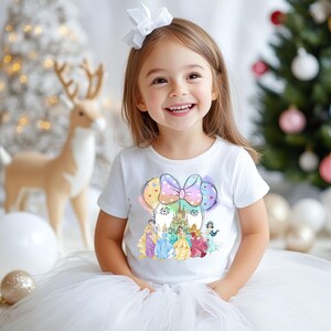 May include: A white t-shirt with a colorful graphic of a Minnie Mouse head with a bow, featuring Disney princesses and Cinderella's castle. The graphic is surrounded by colorful balloons.