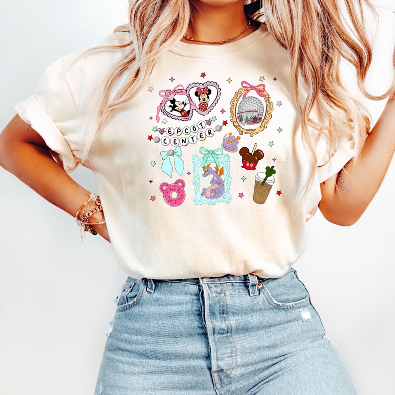 May include: A white t-shirt with a colorful graphic design featuring Mickey Mouse and Minnie Mouse, a castle, a dragon, a donut, and a coffee cup. The text "EPCOT CENTER" is also included in the design.