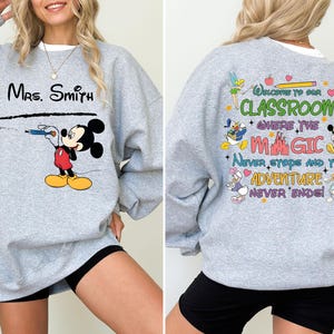 May include: Gray sweatshirt with a Mickey Mouse design on the front and a Disney-themed quote on the back. The quote reads "Welcome to our classroom where the magic never stops and the adventure never ends!"