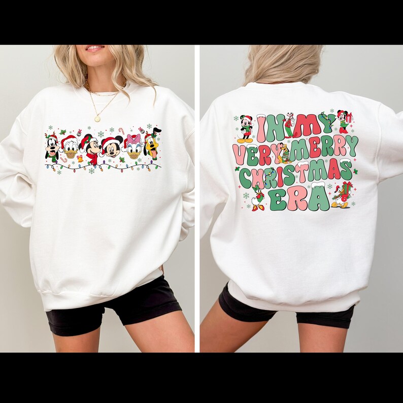 May include: White sweatshirt with a Christmas-themed design featuring Mickey Mouse and other Disney characters. The front of the sweatshirt has a line of characters with Christmas lights and snowflakes. The back of the sweatshirt has the text "In My Very Merry Christmas Era" with characters around the text.