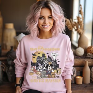May include: A pink sweatshirt with a graphic of Mickey Mouse and friends in front of the Haunted Mansion at Walt Disney World. The text "Walt Disney World" and "The Haunted Mansion" are printed on the shirt.