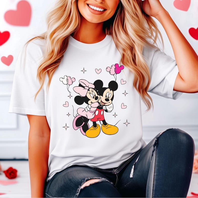 May include: White t-shirt with a graphic of Mickey Mouse and Minnie Mouse hugging, surrounded by pink hearts and stars. The characters are holding pink balloons.