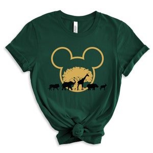 May include: Green t-shirt with a gold Mickey Mouse head silhouette. Inside the silhouette is a gold tree with black silhouettes of a lion, elephant, giraffe, hippopotamus, and zebra.