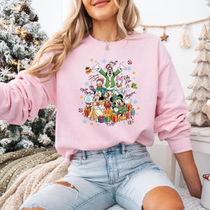 K&ouml;nnte beinhalten: Hellrosa Sweatshirt mit einem festlichen Disney-Motiv. Das Design zeigt Micky und Minnie Maus, Donald und Daisy Duck, Goofy und Pluto, mit Weihnachtselementen wie Geschenken und Schneeflocken. Das Sweatshirt hat eine lockere Passform.