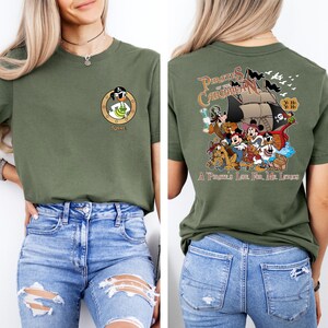 May include: A green t-shirt with a cartoon image of a pirate duck on the front and a group of Disney characters on the back. The back of the shirt says "Pirates of the Caribbean" and "A Pirate's Life for Me, Lads".
