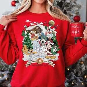 Pu&ograve; includere: Maglione rosso di Natale con una scena invernale con Topolino, Minnie Mouse, Paperino, Pippo e Pluto. I personaggi sono riuniti intorno a una capanna con un albero di Natale e la neve. Il testo "Happiest Place On Earth" e "Walt Disney World" &egrave; stampato sul maglione.