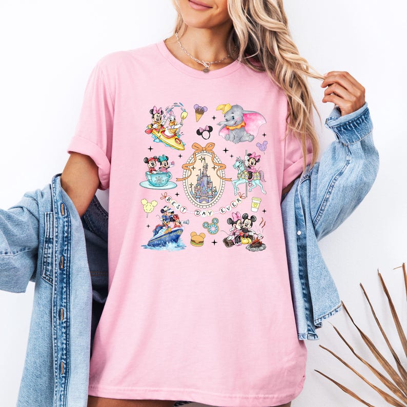 May include: Pink t-shirt with a graphic print of various Disney characters, including Mickey Mouse, Minnie Mouse, Donald Duck, and Goofy. The text "Best Day Ever" is printed on the shirt.