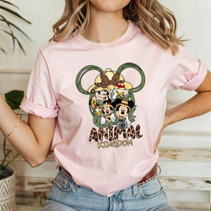 May include: Pink t-shirt with a graphic of Mickey Mouse and friends in a jungle setting. The graphic is inside a Mickey Mouse ear shape. The text "Animal Kingdom" is below the graphic.