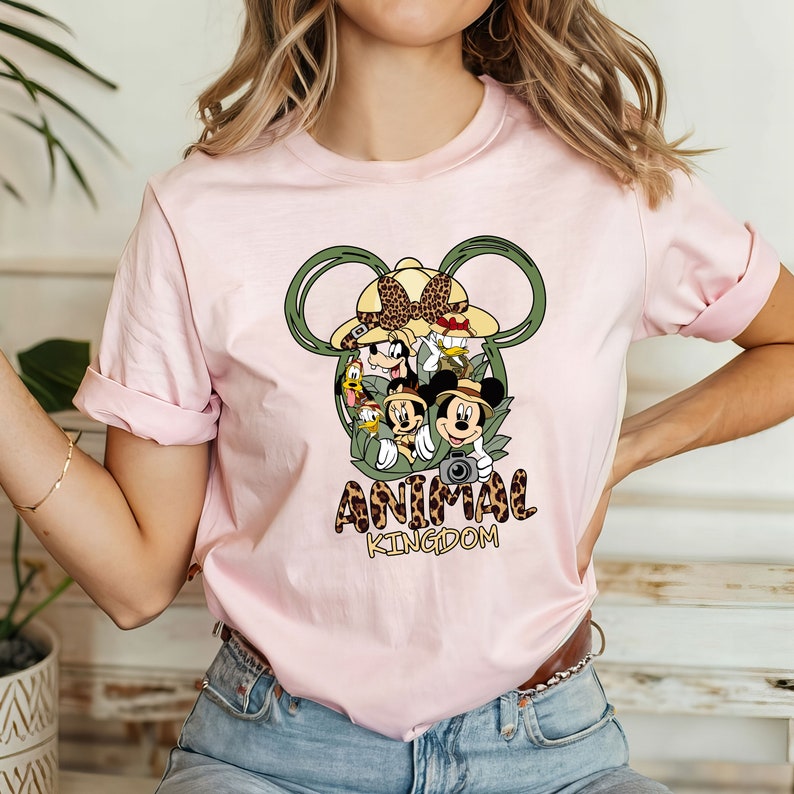 May include: Pink t-shirt with a graphic of Mickey Mouse and friends in a jungle setting. The graphic is inside a Mickey Mouse ear shape. The text "Animal Kingdom" is below the graphic.