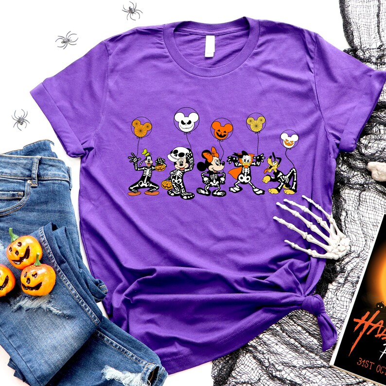 Op de afbeelding: Paars T-shirt met een afbeelding van Mickey Mouse, Minnie Mouse, Donald Duck, Goofy en Pluto verkleed als skeletten die Halloween-ballonnen vasthouden.