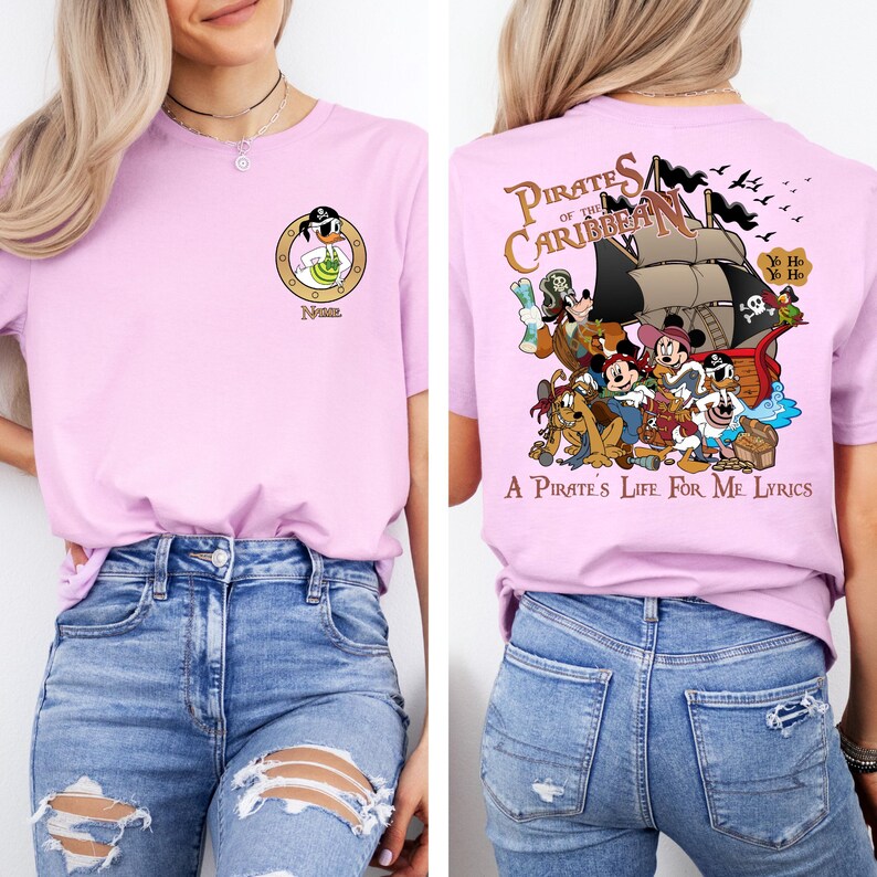 May include: Pink t-shirt with a cartoon pirate character on the front and a graphic of Mickey Mouse and friends on a pirate ship on the back. The back graphic includes the text "Pirates of the Caribbean" and "A Pirate's Life for Me Lyrics".