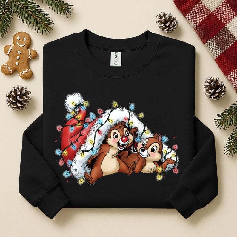 May include: Black sweatshirt featuring Chip and Dale characters with a Santa hat and Christmas lights. The design includes a gingerbread man, pine cones, and evergreen branches, creating a festive holiday theme.