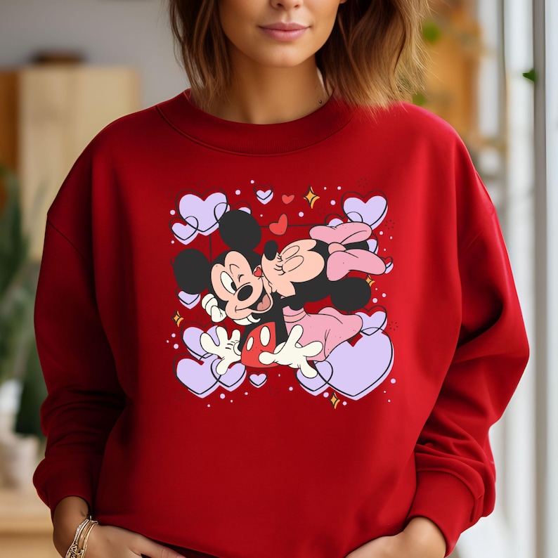 May include: Red sweatshirt with a graphic print of Mickey Mouse and Minnie Mouse kissing surrounded by purple hearts.