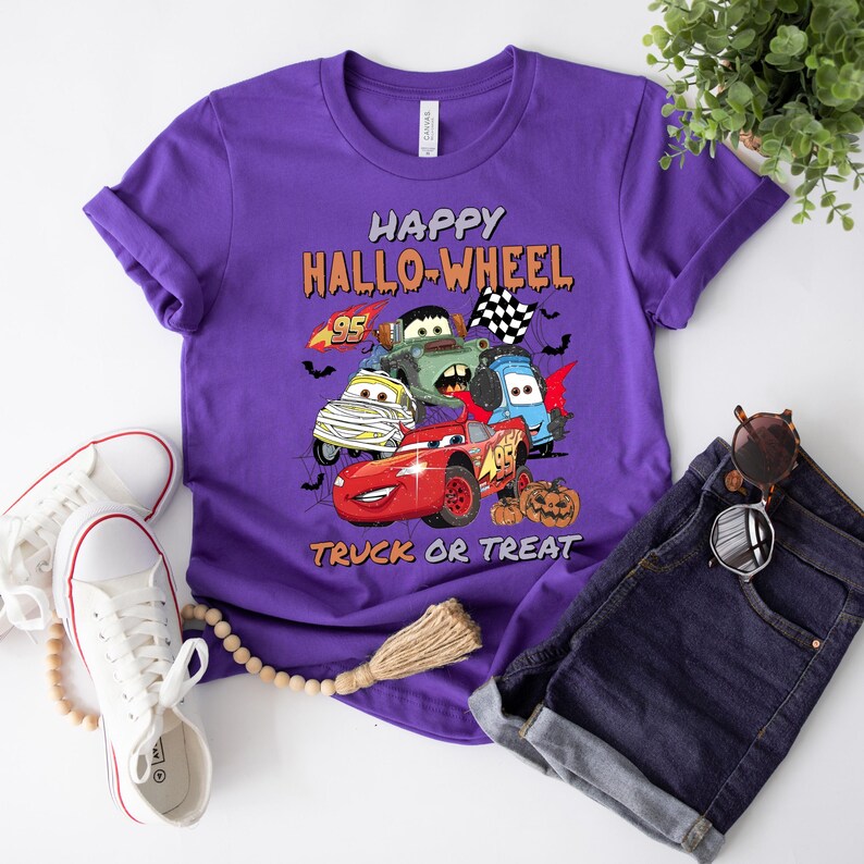 May include: Purple t-shirt with a graphic of cartoon cars and the text "Happy Hallo-Wheel Truck or Treat".