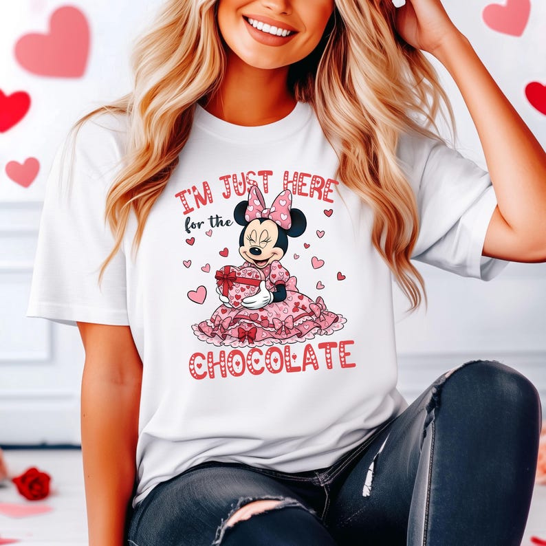 May include: White t-shirt featuring a cartoon Minnie Mouse in a pink dress holding a heart-shaped gift box. The text "I'M JUST HERE for the CHOCOLATE" is printed in red. Hearts are scattered around the design.