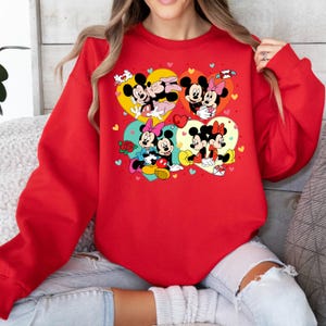 May include: Red sweatshirt with a graphic print of Mickey Mouse and Minnie Mouse in various poses. The graphic features hearts, flowers, and other Valentine's Day themed elements.