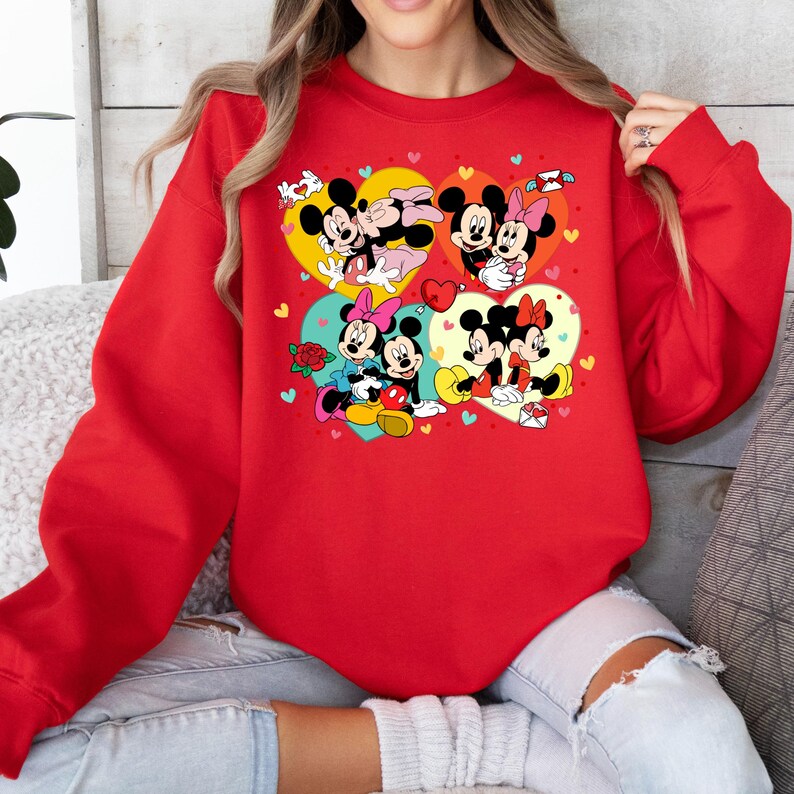 May include: Red sweatshirt with a graphic print of Mickey Mouse and Minnie Mouse in various poses. The graphic features hearts, flowers, and other Valentine's Day themed elements.