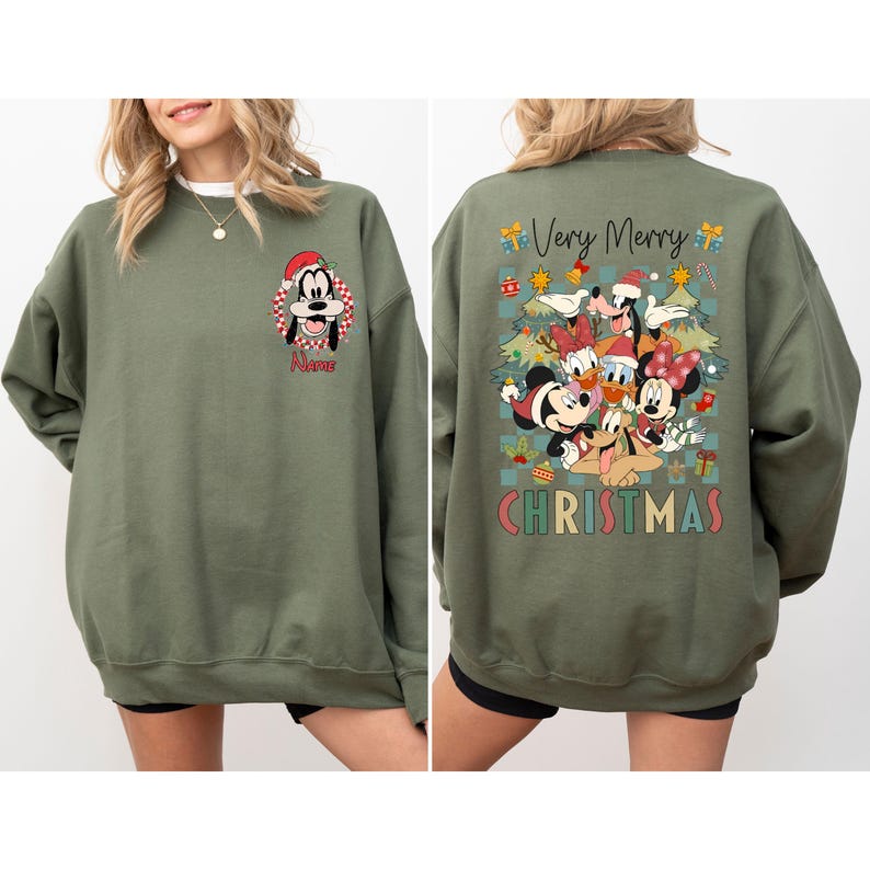 May include: Olive green sweatshirt featuring a Christmas-themed graphic. The front displays a cartoon of Goofy in a Santa hat with the name "Name" below. The back showcases Mickey, Minnie, Donald, Daisy, and Pluto with "Very Merry Christmas" text.