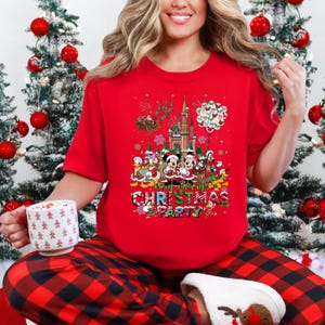 May include: Red t-shirt with a colorful graphic featuring Disney characters, a castle, and the text "Very Merry Christmas Party." The design includes Mickey and Minnie Mouse, Donald Duck, and other characters. The person is wearing red and black plaid pajama pants.