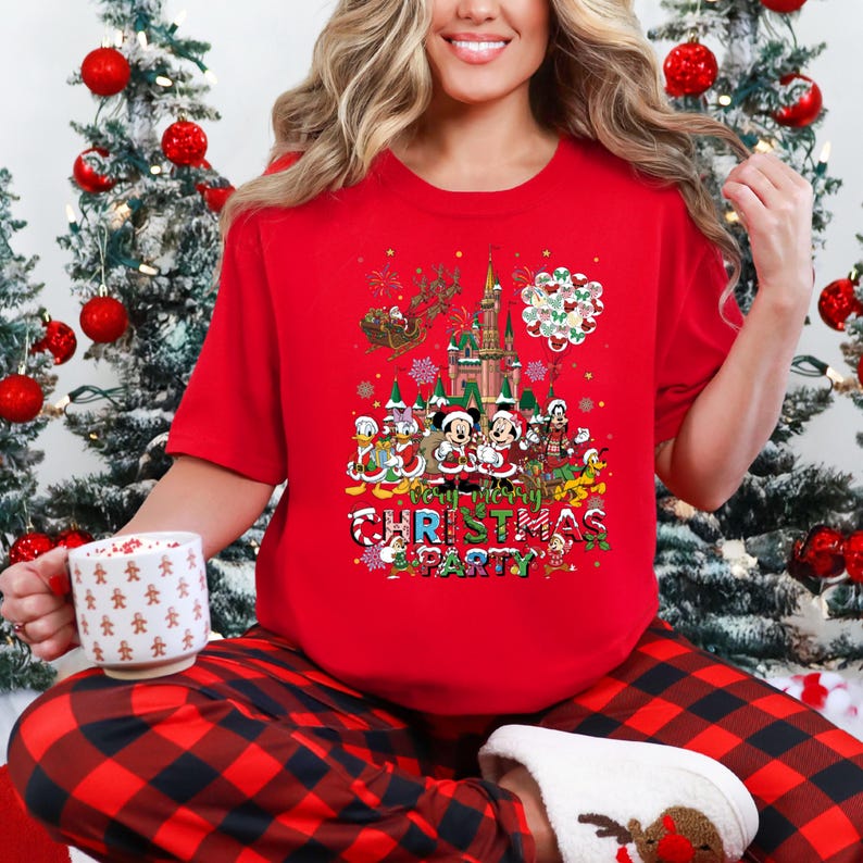 May include: Red t-shirt with a colorful graphic featuring Disney characters, a castle, and the text "Very Merry Christmas Party." The design includes Mickey and Minnie Mouse, Donald Duck, and other characters. The person is wearing red and black plaid pajama pants.
