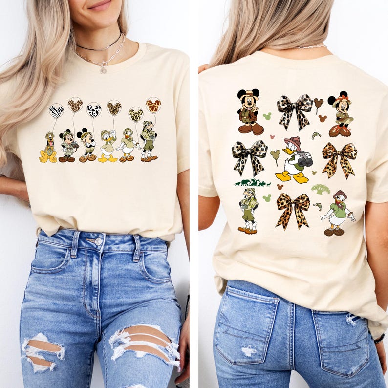 May include: A beige t-shirt with a graphic print of Disney characters dressed in safari outfits. The characters are holding balloons with animal print designs. The back of the shirt has a repeating pattern of the same characters and bows with animal print designs.