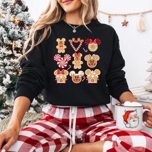 May include: Black sweatshirt with a Christmas gingerbread design featuring Mickey Mouse and friends. The design includes gingerbread men, candy canes, and gingerbread houses.