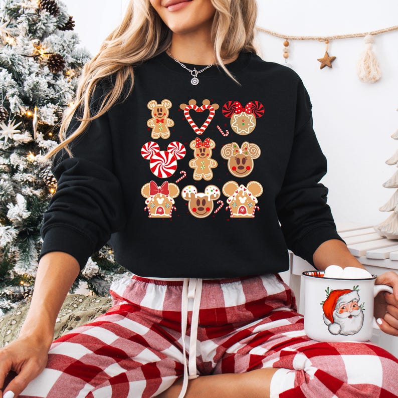 May include: Black sweatshirt with a Christmas gingerbread design featuring Mickey Mouse and friends. The design includes gingerbread men, candy canes, and gingerbread houses.