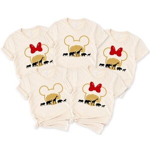 May include: Set of five beige t-shirts with a gold Mickey Mouse head silhouette and a red bow. Each shirt features a silhouette of a giraffe, elephant, lion, zebra, and rhino.