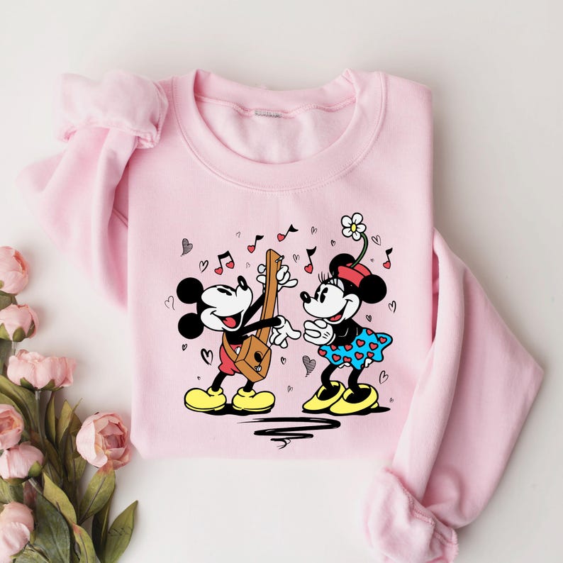 Pode incluir: Camisola rosa com uma estampa gr&aacute;fica de Mickey Mouse e Minnie Mouse tocando m&uacute;sica. Mickey Mouse est&aacute; tocando guitarra e Minnie Mouse est&aacute; segurando uma flor.
