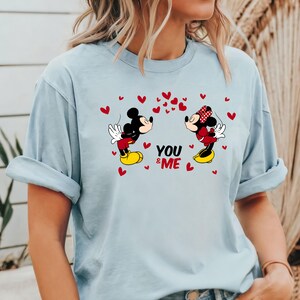 May include: Light blue t-shirt with a graphic of Mickey Mouse and Minnie Mouse kissing. The graphic is surrounded by red hearts and the text "YOU & ME".