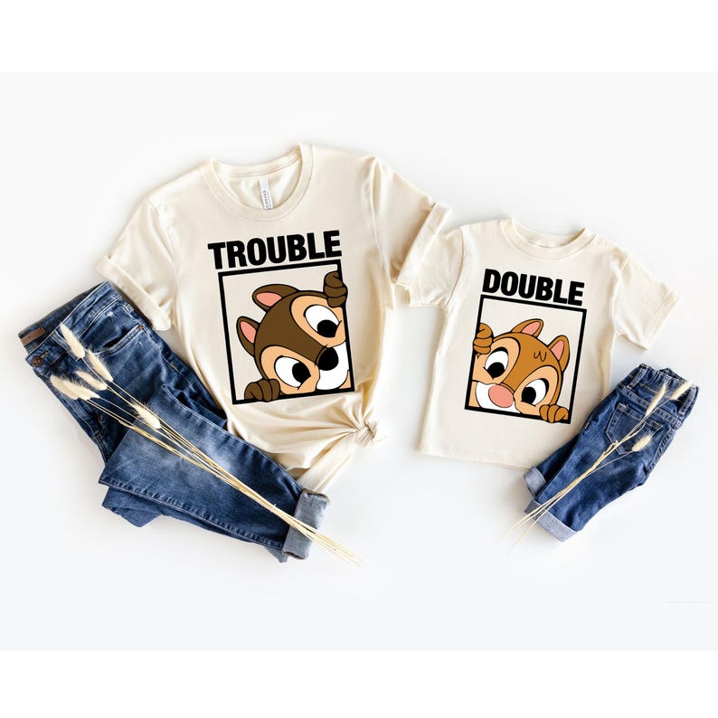 May include: Two beige t-shirts with a cartoon chipmunk peeking out of a box. The larger shirt says "Trouble" and the smaller shirt says "Double".