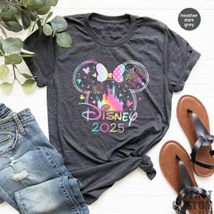 May include: A heather dark grey t-shirt with a rainbow-colored Mickey Mouse ears design and the text "DISNEY 2025".