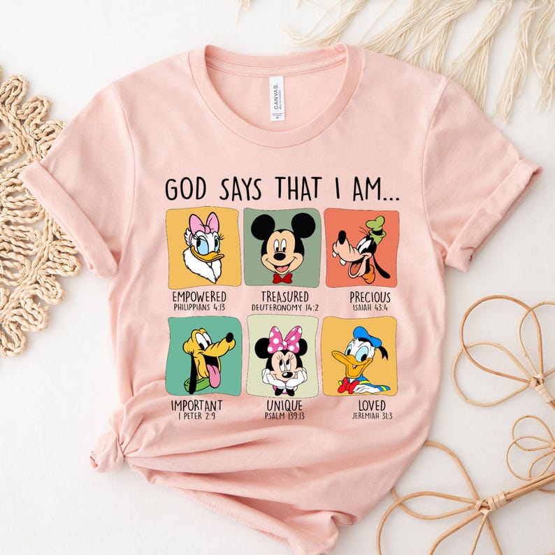 Puede incluir: Una camiseta rosa claro con el texto "GOD SAYS THAT I AM..." encima de seis retratos de personajes de dibujos animados. Cada retrato tiene una palabra y un vers&iacute;culo b&iacute;blico correspondientes. Los personajes incluyen a Daisy Duck, Mickey Mouse, Goofy, Pluto, Minnie Mouse y Donald Duck.