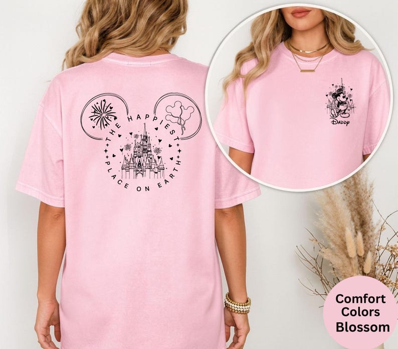 May include: A light pink t-shirt with a graphic of a castle, fireworks, and balloons inside a Mickey Mouse head shape. The text "THE HAPPIEST PLACE ON EARTH" is printed around the design. A smaller graphic of Mickey Mouse is on the front.