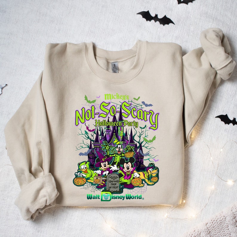 May include: A beige sweatshirt with a green, purple, and black graphic print of Mickey Mouse and friends in front of a castle. The text "Mickey's Not-So-Scary Halloween Party" is printed on the sweatshirt. The text "Walt Disney World" is printed at the bottom of the graphic.