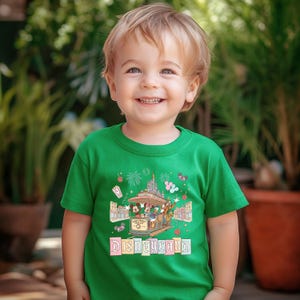 May include: A green t-shirt featuring a Disneyland graphic. The graphic includes a trolley with Mickey Mouse, Donald Duck, and other characters, fireworks, and the word "Disneyland" in a colorful font. The shirt is worn by a young child.