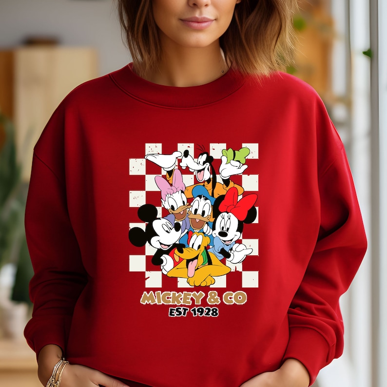 Puede incluir: Sudadera roja con un patr&oacute;n a cuadros con Mickey Mouse y sus amigos. El texto "Mickey & Co. Est 1928" est&aacute; impreso debajo de la imagen.