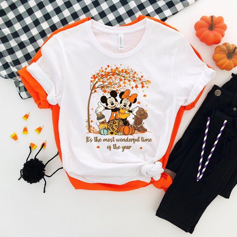 May include: White t-shirt with a fall graphic featuring Mickey and Minnie Mouse, pumpkins, and a tree with orange leaves. The text reads "It's the most wonderful time of the year."