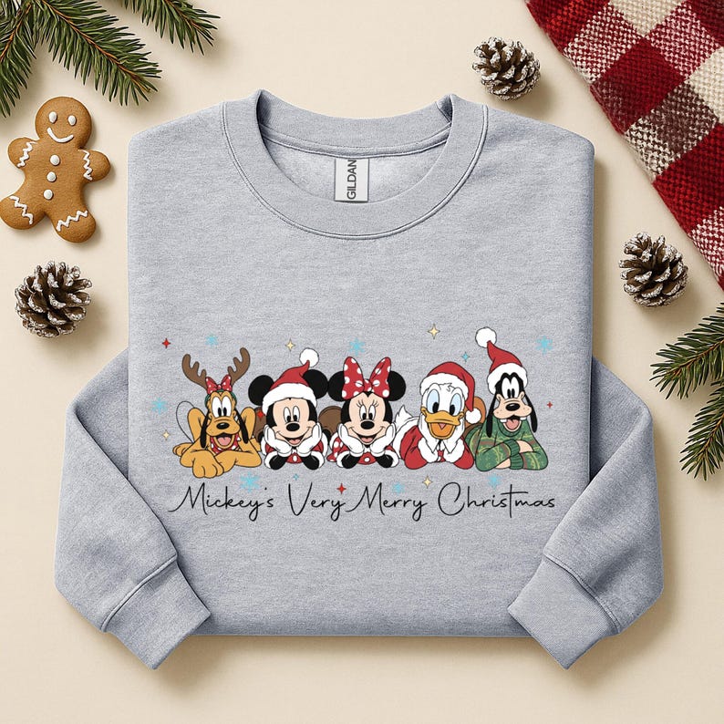 Puede incluir: Una sudadera gris claro con personajes de Disney con atuendos navide&ntilde;os. El dise&ntilde;o incluye a Pluto con cuernos de reno, Mickey Mouse, Minnie Mouse, el Pato Donald y Goofy. El texto "Mickey's Very Merry Christmas" est&aacute; escrito en cursiva.