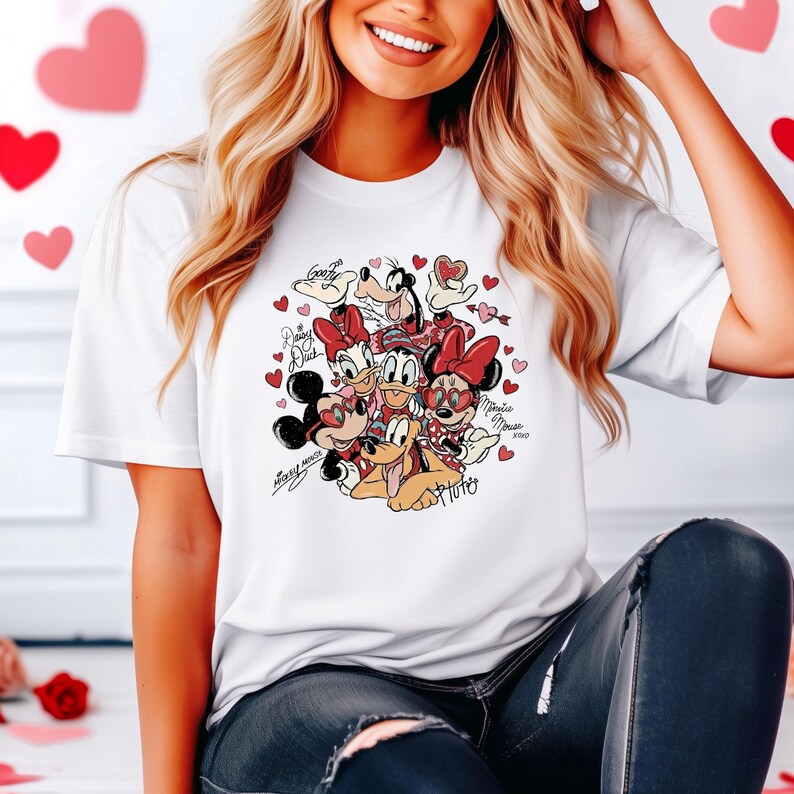 May include: White t-shirt featuring a graphic of Disney characters including Mickey and Minnie Mouse, Donald and Daisy Duck, Goofy, and Pluto, surrounded by hearts. The shirt has the names of the characters written on it.