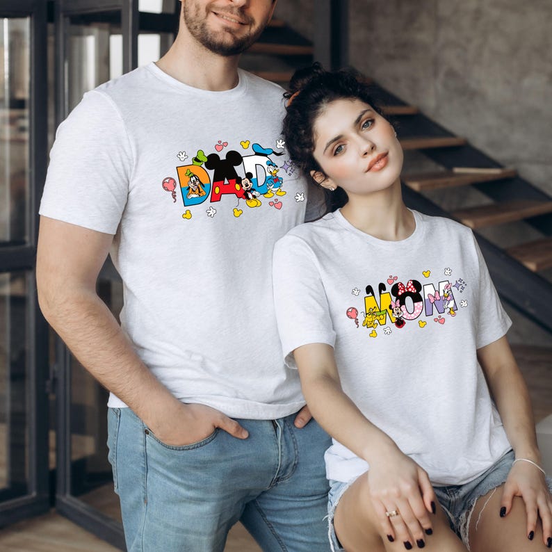 May include: White t-shirts with a graphic design featuring Disney characters spelling out "DAD" and "MOM".