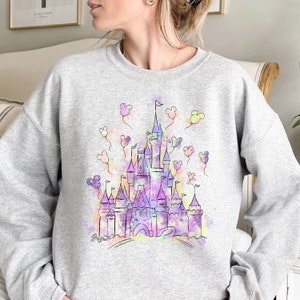 May include: A grey sweatshirt featuring a watercolour illustration of a castle with Mickey Mouse ears floating around it.