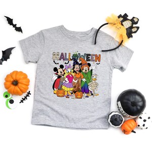 May include: A gray short-sleeved t-shirt featuring a Halloween graphic with cartoon characters dressed in costumes. The word "HALLOWEEN" is printed across the front. Decorative pumpkins and bats are also present.