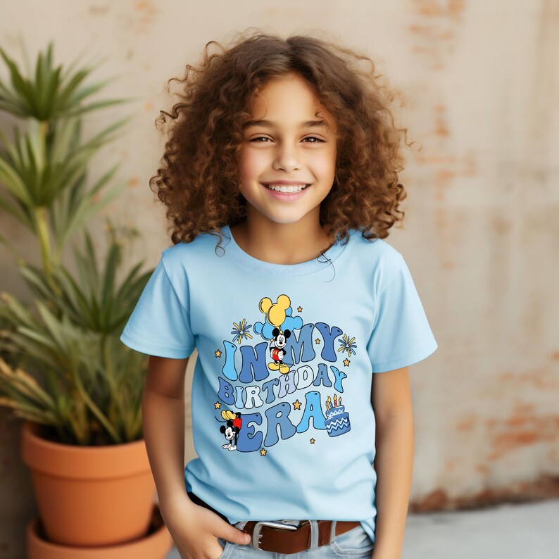 May include: A light blue t-shirt with a graphic of Mickey Mouse and the text "In My Birthday Era".
