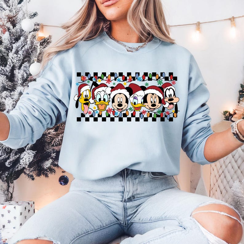 May include: Light blue sweatshirt with a checkered pattern and a row of Disney characters wearing Santa hats. The characters include Mickey Mouse, Minnie Mouse, Donald Duck, Goofy, and Pluto.
