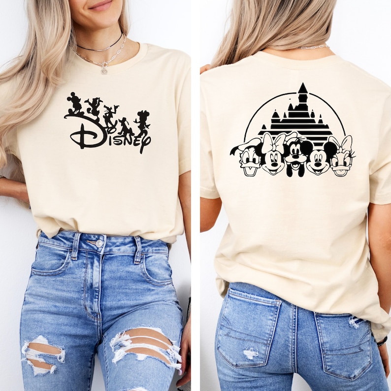 Puede incluir: Una camiseta beige con un logotipo de Disney negro y personajes en la parte delantera y una silueta negra del castillo de Disney con Mickey Mouse y sus amigos en la parte posterior.